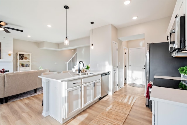 kitchen featuring a center island with sink, sink, white cabinetry, hanging light fixtures, and stainless steel appliances