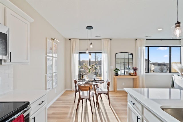 kitchen with decorative light fixtures, white cabinets, and light hardwood / wood-style flooring