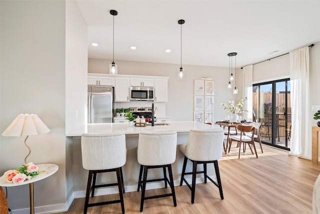 kitchen featuring hanging light fixtures, white cabinets, a kitchen breakfast bar, and stainless steel appliances