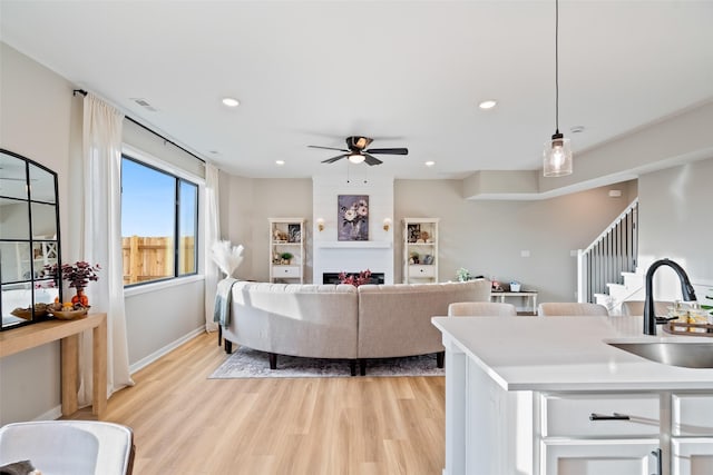 living room featuring light wood-type flooring, ceiling fan, a fireplace, and sink