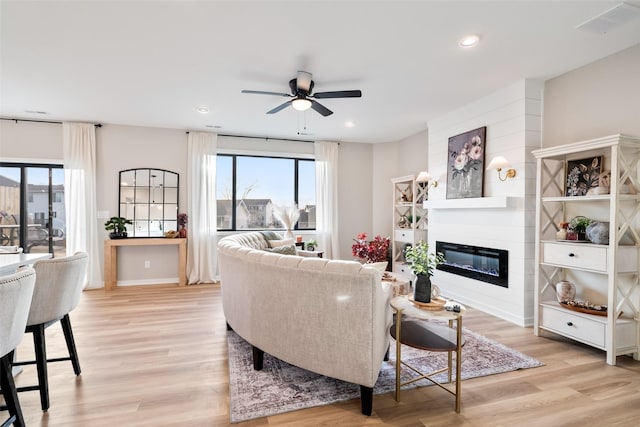 living room featuring ceiling fan, a large fireplace, light hardwood / wood-style flooring, and plenty of natural light