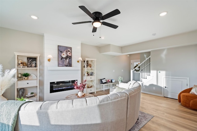 living room with ceiling fan, light hardwood / wood-style floors, and a large fireplace