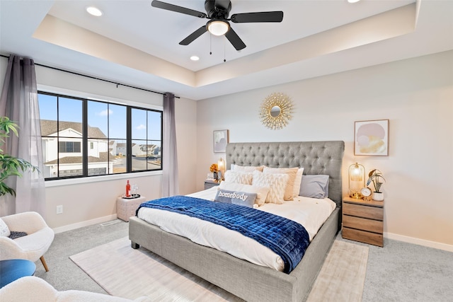 bedroom with ceiling fan, a tray ceiling, and light carpet