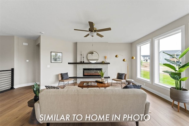 living room featuring wood-type flooring, ceiling fan, and a tiled fireplace