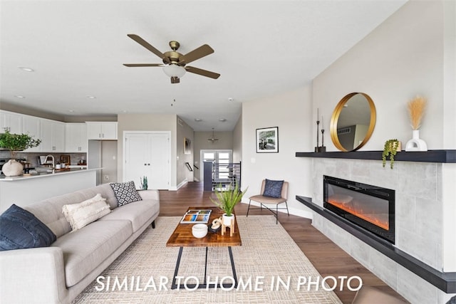 living room with hardwood / wood-style floors, ceiling fan, and a tiled fireplace