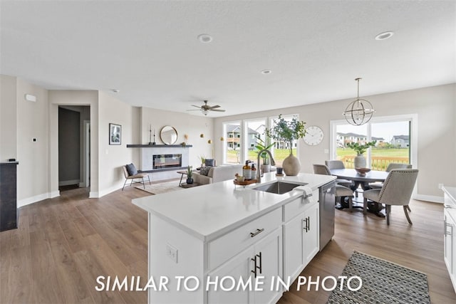 kitchen with a kitchen island with sink, sink, hanging light fixtures, white cabinetry, and wood-type flooring