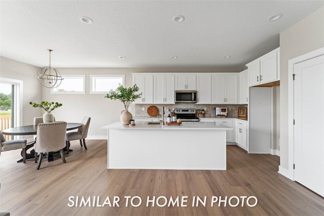 kitchen featuring light wood-type flooring, stainless steel appliances, white cabinetry, and a kitchen island with sink