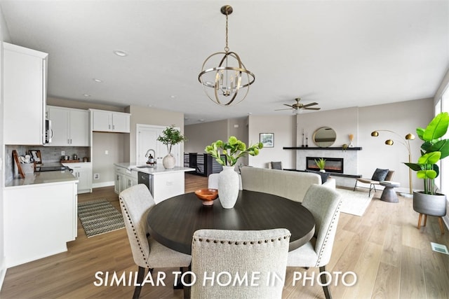 dining area featuring a fireplace, sink, light hardwood / wood-style floors, and ceiling fan with notable chandelier