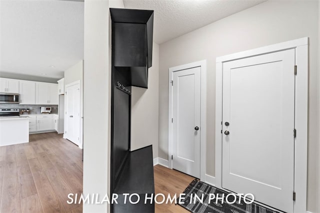 interior space featuring white cabinetry, white electric range, tasteful backsplash, light hardwood / wood-style flooring, and a textured ceiling