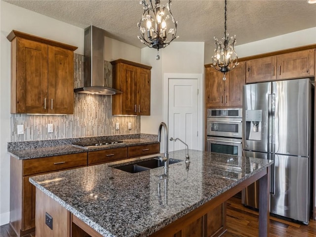 kitchen featuring tasteful backsplash, wall chimney range hood, dark stone counters, stainless steel appliances, and a sink