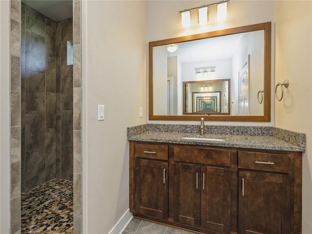 bathroom featuring a tile shower, vanity, and baseboards