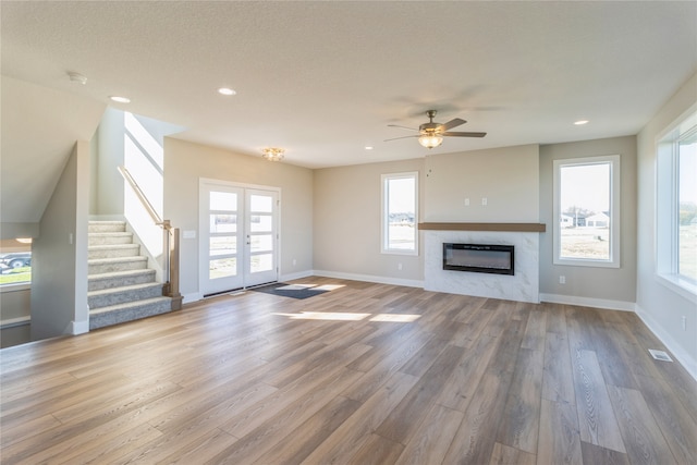 unfurnished living room featuring ceiling fan, wood-type flooring, a wealth of natural light, and a high end fireplace