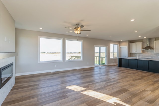 unfurnished living room with a wealth of natural light, a tiled fireplace, light wood-type flooring, and ceiling fan