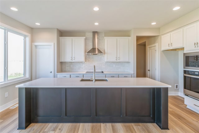 kitchen with wall chimney range hood, white cabinetry, a kitchen island with sink, and appliances with stainless steel finishes