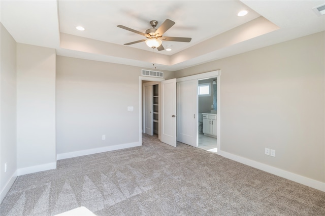 unfurnished bedroom with a closet, ceiling fan, light carpet, and a tray ceiling