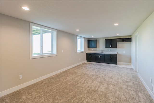 unfurnished living room with sink, light colored carpet, and plenty of natural light