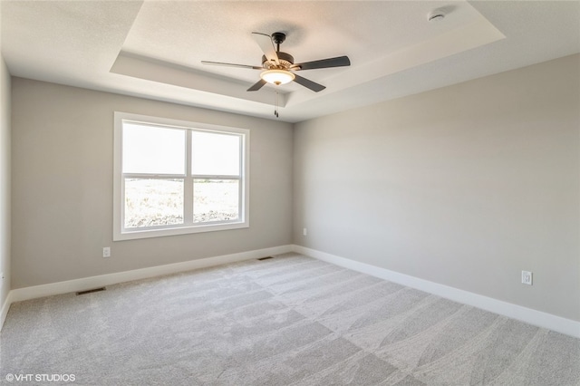 carpeted spare room with a tray ceiling and ceiling fan