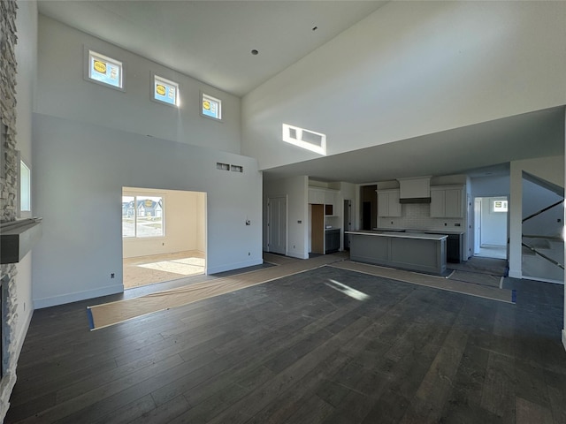 unfurnished living room featuring dark hardwood / wood-style floors, a stone fireplace, and a towering ceiling