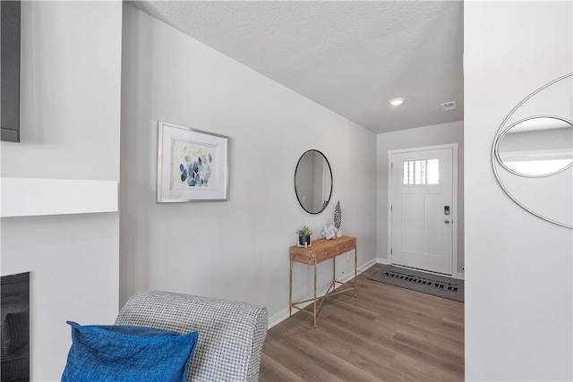 foyer featuring a textured ceiling, wood finished floors, visible vents, and baseboards