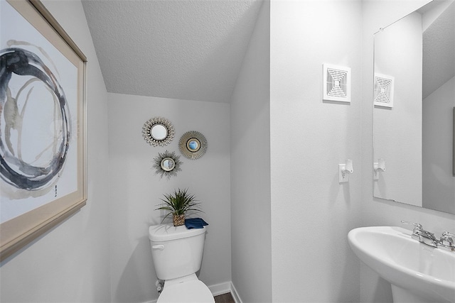 bathroom with a textured ceiling, a sink, toilet, and lofted ceiling