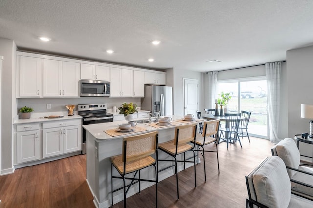 kitchen with appliances with stainless steel finishes, a kitchen breakfast bar, wood finished floors, light countertops, and white cabinetry