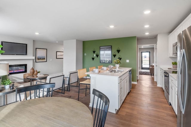 kitchen featuring white cabinets, a glass covered fireplace, a kitchen island, stainless steel appliances, and light countertops