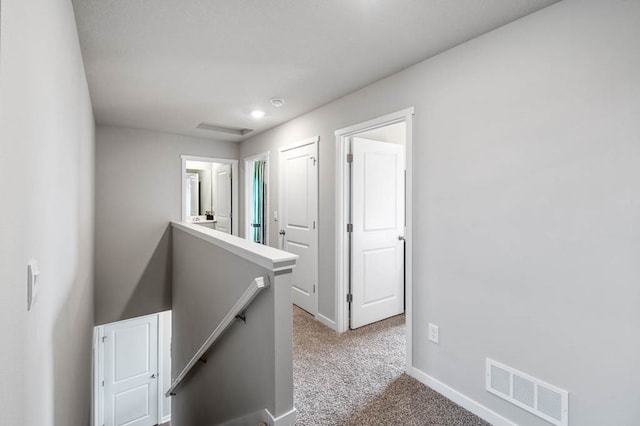 hallway featuring baseboards, visible vents, carpet flooring, and an upstairs landing