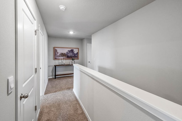 hall featuring baseboards, an upstairs landing, and light colored carpet