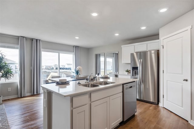 kitchen featuring appliances with stainless steel finishes, an island with sink, sink, hardwood / wood-style flooring, and white cabinets