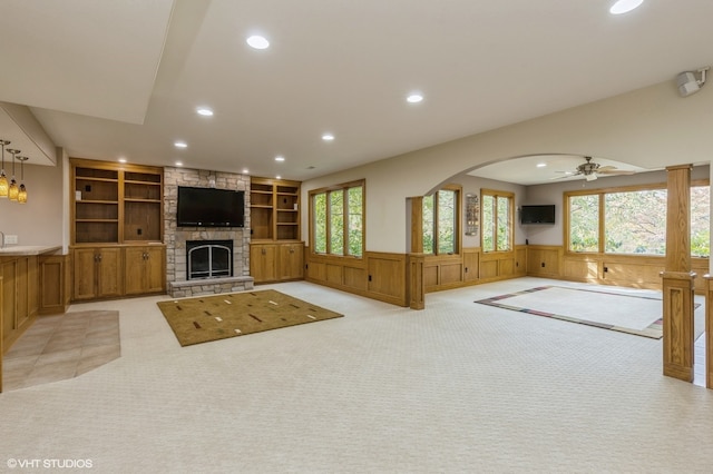 unfurnished living room with wooden walls, light colored carpet, a healthy amount of sunlight, and ceiling fan