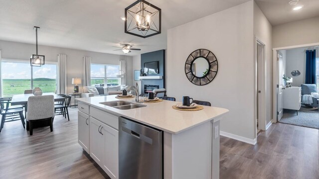 kitchen featuring a kitchen island with sink, stainless steel dishwasher, wood-type flooring, sink, and pendant lighting