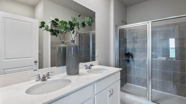 bathroom featuring a shower with door, dual sinks, and large vanity