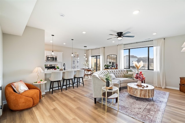 living room featuring ceiling fan, sink, and light hardwood / wood-style flooring