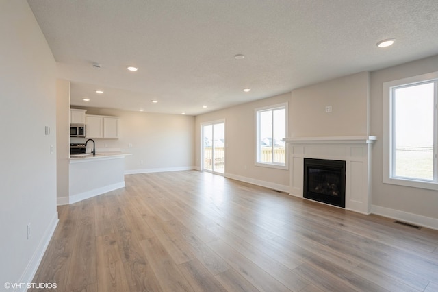 unfurnished living room with sink, a textured ceiling, and light wood-type flooring