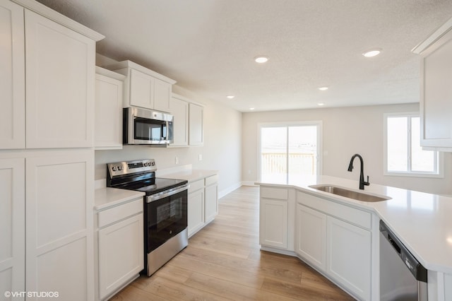 kitchen with white cabinetry, a textured ceiling, light hardwood / wood-style flooring, sink, and stainless steel appliances