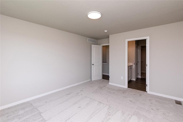 unfurnished bedroom featuring ensuite bath, light carpet, and a textured ceiling