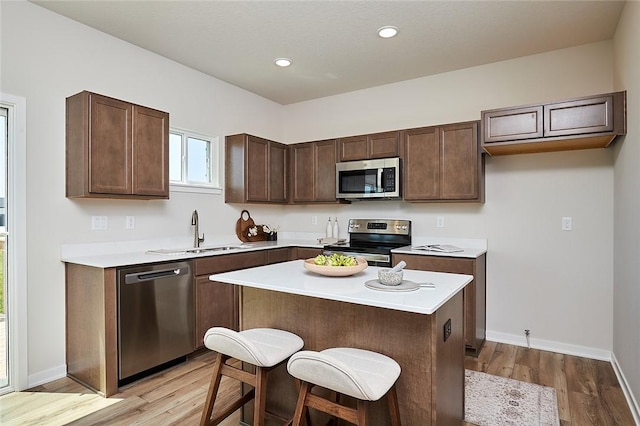 kitchen with a center island, sink, a breakfast bar area, light hardwood / wood-style flooring, and appliances with stainless steel finishes