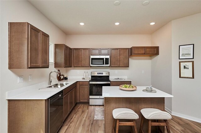 kitchen with sink, a kitchen island, stainless steel appliances, a breakfast bar, and light hardwood / wood-style floors