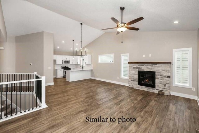 unfurnished living room featuring ceiling fan with notable chandelier, a fireplace, vaulted ceiling, and plenty of natural light