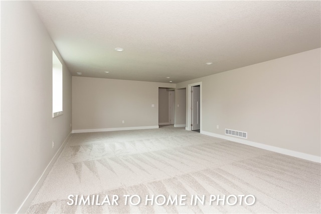 empty room featuring a textured ceiling, light carpet, visible vents, and baseboards