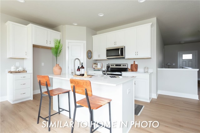 kitchen with appliances with stainless steel finishes, a breakfast bar, a kitchen island with sink, light countertops, and white cabinetry