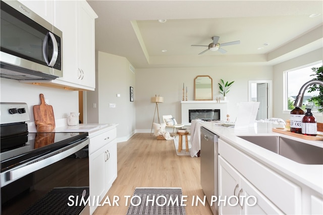 kitchen featuring white cabinets, a raised ceiling, stainless steel appliances, light countertops, and a sink