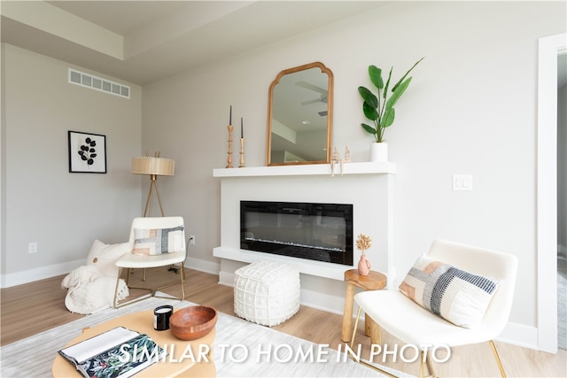 sitting room featuring a glass covered fireplace, visible vents, baseboards, and wood finished floors