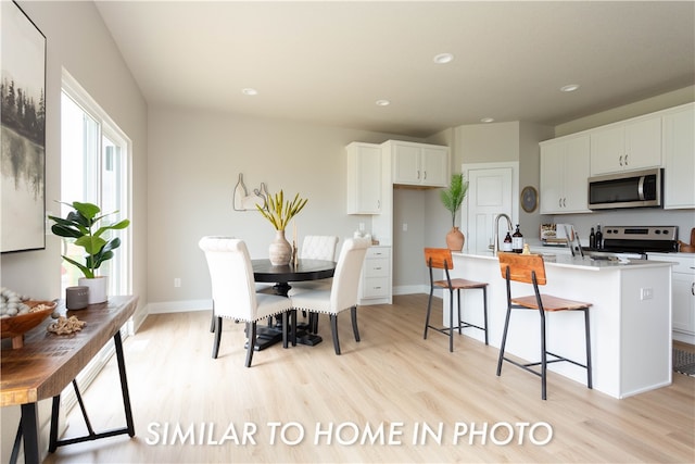 kitchen with a kitchen island with sink, white cabinetry, light countertops, appliances with stainless steel finishes, and light wood-type flooring