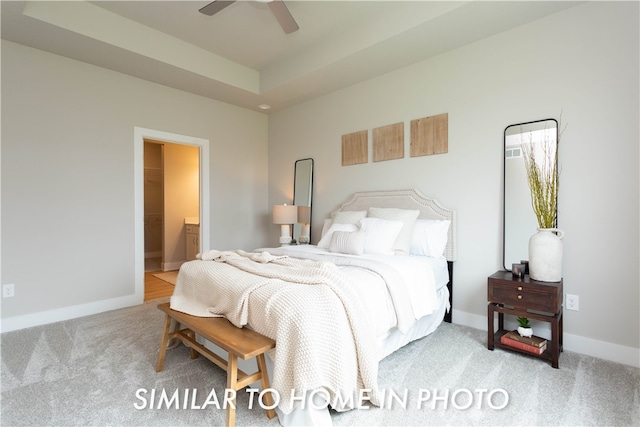 bedroom with carpet floors, a tray ceiling, ensuite bath, and baseboards