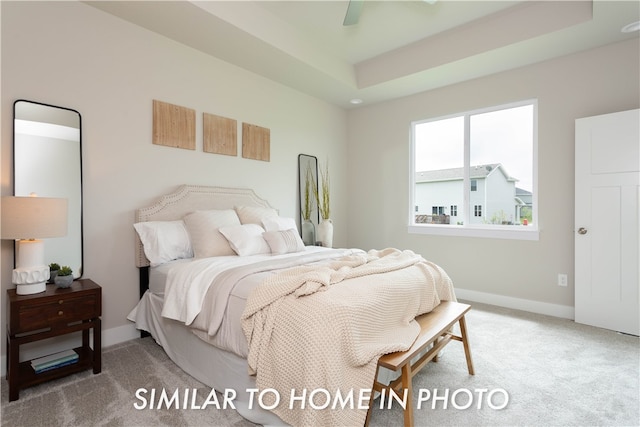 carpeted bedroom with ceiling fan, a raised ceiling, and baseboards