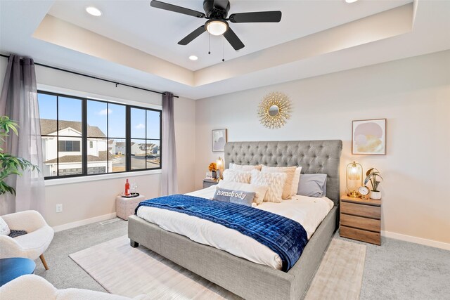 bedroom with ceiling fan, light colored carpet, and a tray ceiling