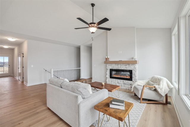 living room featuring ceiling fan, vaulted ceiling, a stone fireplace, and light hardwood / wood-style flooring