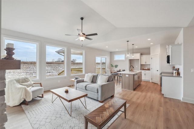 living room featuring ceiling fan, light hardwood / wood-style flooring, vaulted ceiling, and sink