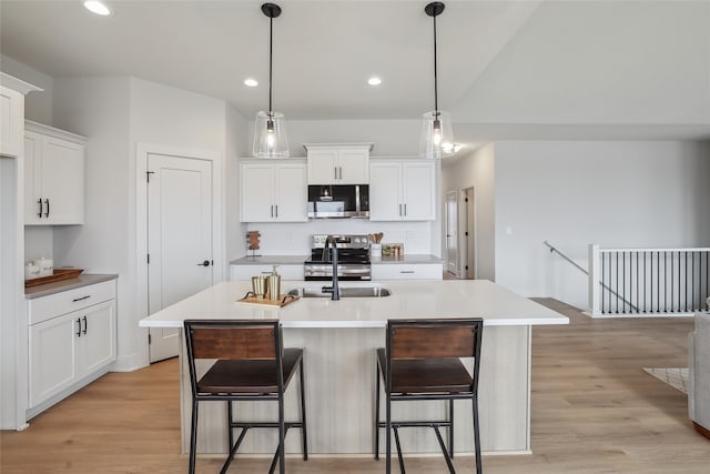 kitchen featuring appliances with stainless steel finishes, sink, decorative light fixtures, white cabinets, and an island with sink